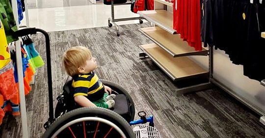 Junge im Rollstuhl bleibt mitten im Spielwarenladen vor Plakat stehen, weil er sich selbst wiedererkennt