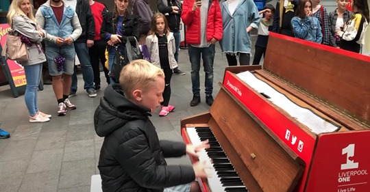 Junge sitzt am Klavier und spielt ein vierminütiges Medley von Tanzhits, das eine riesige Menschenmenge begeistert.