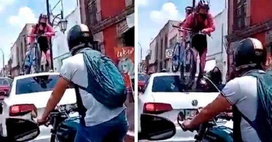 Ein Auto blockiert den Radweg: eine Radfahrerin klettert mit ihrem ganzen Fahrrad darauf, um durchzukommen